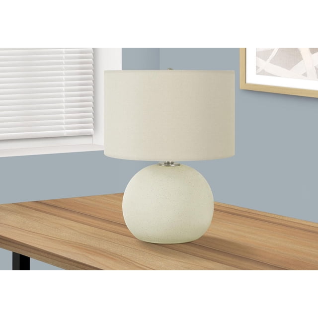 Monarch Specialties Lighting 18-inch table lamp with a textured cream ceramic globe base and ivory fabric drum shade topped by a silver finial, placed on a wooden table near a window with white blinds and light blue walls, ideal for adjustable ambient lighting with a 3-way switch.