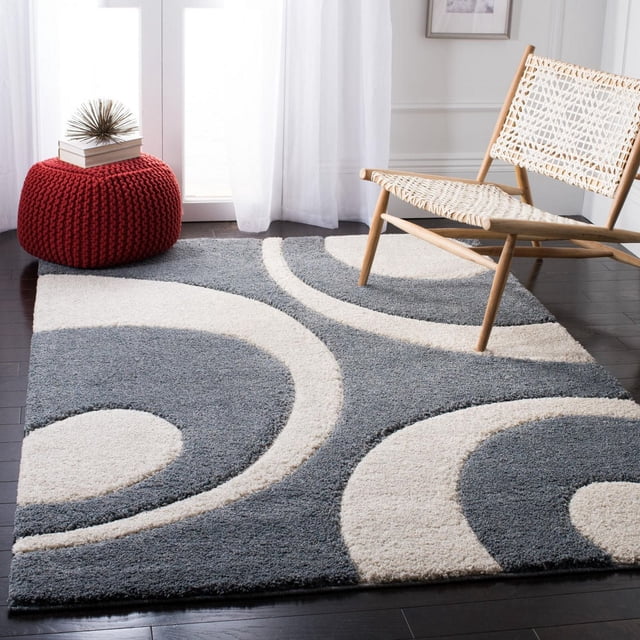 Safavieh Florida Mirabelle Tapis Shag Contemporain pour Aire, Présentant une Peluche à Poils Longs et Courts avec des Motifs Tourbillonnants Abstraits Gris et Crème sur un Plancher de Bois Franc Foncé, Style avec une Chaise en Bois Tressé et un pouf Tricoté Rouge avec des Livres, Convient pour Améliorer la texture et le Confort dans les Aires de Vie.