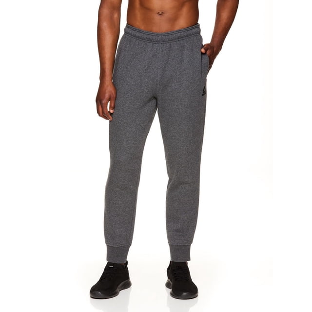 Reebok Jogger en Molleton Delta pour Homme en Molleton Gris Foncé Coton-Polyester avec Jambes Fuselées, Taille Élastique avec Cordon de Serrage de Marque, Poignets Côtelés, Deux Poches Latérales Ouvertes, une Poche de Hanche Zippée et un logo Reebok Noir sur la Cuisse Gauche, Conçu par un Homme Sans Chemise sur Fond Blanc, Convient à une Tenue Décontractée Ou à un Usage Actif.