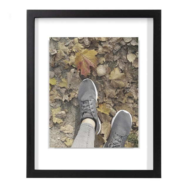 hometrends Gallery Float Black Picture Frame showing a centered photo of feet wearing gray sneakers standing on dry autumn leaves, with a black frame and white mat holding an 11 by 14 inch photo, ideal for home or office wall decoration.