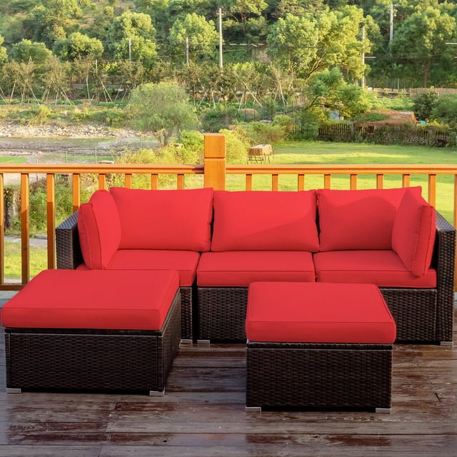 Gymax Ensemble de Conversation de Patio en Rotin 5 Pcs Ensemble de Meubles d'Extérieur avec Ottoman Comprenant Deux Canapés d'Angle, un sofa Sans Accoudoirs et Deux ottomans. Fabriqué avec un Rotin PE durable et un Cadre en Acier Robuste, l'Ensemble Comprend des Coussins Rouge Vif pour le Confort. les ottomans Peuvent Être Convertis en table Basse en Enlevant les Coussins. Parfait pour les Espaces Extérieurs comme les patios, les porches Ou les Zones au Bord de la Piscine. Exposé sur une Terrasse en Bois avec un Paysage Vert Luxuriant en Arrière-Plan.