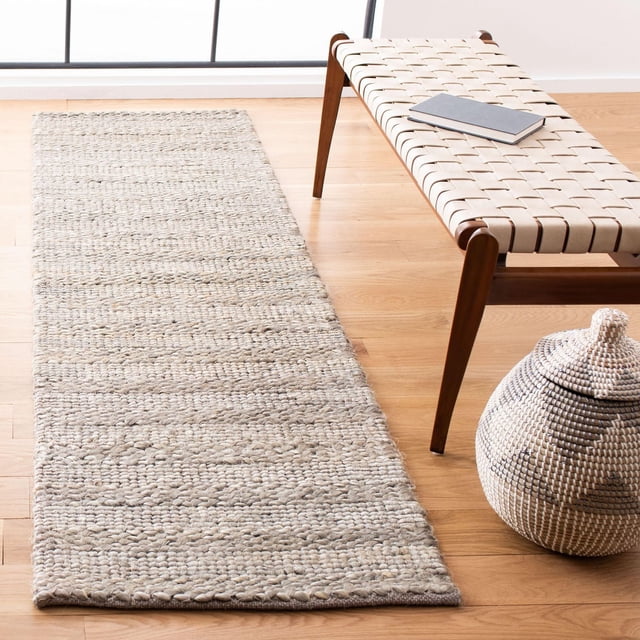 Safavieh Tapis d'Aire Tressé en Fibre Naturelle Henrika en beige Naturel, Présenté comme un Coureur en sisal Tressé durable sur Plancher de Bois Franc Clair à Côté d'Un Banc à Sangle en Cuir Tressé avec Pattes en Bois et un Livre Fermé, à Côté d'Un Panier Tressé avec Couvercle, Idéal pour un style de Maison de Plage Côtière Ou Décontracté et pour le Couloir.