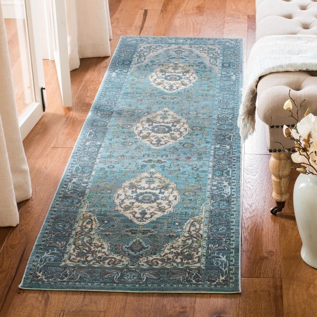 SAFAVIEH Luxor Amadine Tapis à Bordure Florale en Tons Bleus avec un Tissage Égyptien Noué à la Main, Comprenant Trois Médaillons Floraux et une Bordure Complexe, Placé sur un Plancher de Bois Franc à Côté d'Un Banc Capitonné beige et un vase Blanc avec des Fleurs, Idéal pour Rehausser les Zones de Tapis Coureur avec une Élégance Exotique.