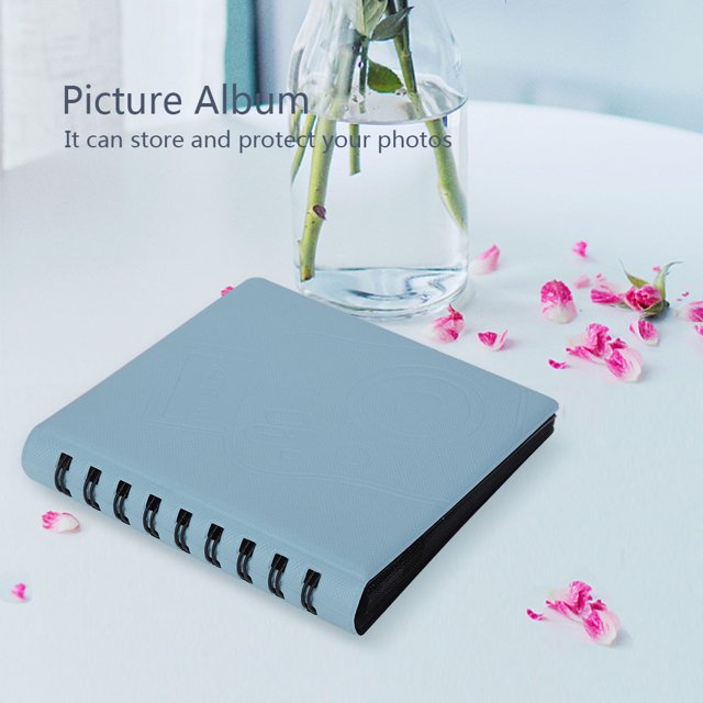 Photograph Album, Picture Case Storage Photo Album Modern Photo Album, Min Photo Album Picture For Child Family. A compact, modern photo album with a light blue PVC and PU cover, featuring a durable spine and 17 inside pages that can hold up to 4 pictures per page. The album measures approximately 13.5x13x2.5cm and is suitable for storing 6x8.8cm photos. Displayed on a white table with scattered pink flower petals and a glass vase in the background.
