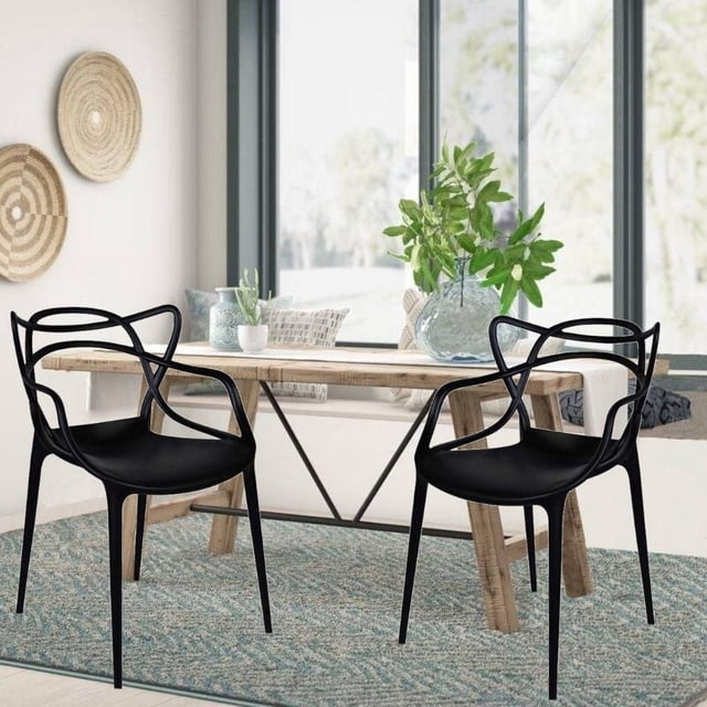 Master Style Plastic Chair Modern Mid Century, Indoor Outdoor Chair Patio Chair Kitchen Chair 18 Inch Seat Height Restaurant Chair Plastic Stackable Chair in Black Set 2 shown in a bright dining area with two black stackable polypropylene chairs featuring open geometric armrests and backrests, placed on a blue-grey textured rug beside a natural wood table with green plants and cushions, ideal for restaurant, kitchen, or patio seating.