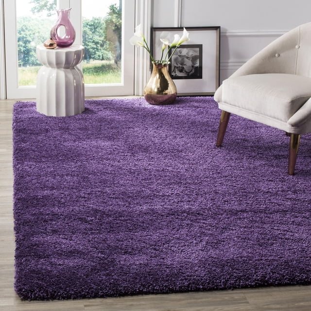 Safavieh Milan Harlow Tapis Shag Uni en Violet Riche, Posé sur un Plancher de Bois Clair dans une Pièce Éclatante avec une table d'Appoint en Céramique Blanche Tenant des vases en Verre et une Chaise Rembourrée beige, Offrant une texture Douce et un accent vibrant pour la Déco Contemporaine de la Maison.