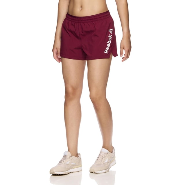 Reebok Women's Staple Running Short with Mesh Lining in burgundy, front view on a model from waist to mid-thigh, made of lightweight polyester with elastic waistband and inside drawcord, side slit, white Reebok Delta logo on left leg, suitable for running or training.
