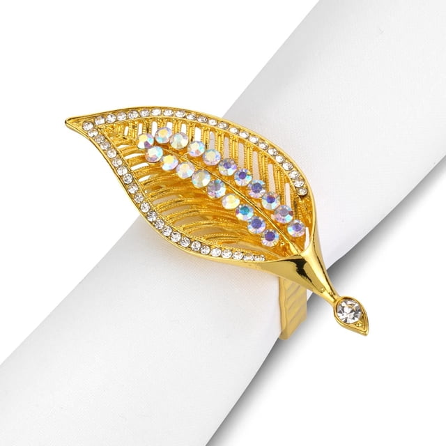 Sparkle Gold Napkin Ring, Set of 4, gold leaf-shaped with intricate cutouts and a border of clear crystals. The center has two rows of iridescent crystals. Shown on a white napkin, perfect for enhancing table linens in dining and entertaining, and suitable as a gift for special occasions.
