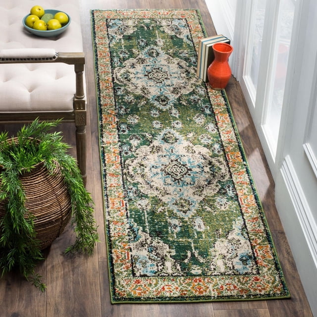 Safavieh Monaco Toria Traditional Area Rug runner with a power-loomed polypropylene weave, displaying a distressed Persian design in green, cream, blue, and orange hues, placed on a hardwood floor beside a beige tufted bench, a wicker basket with greenery, and a red ceramic vase with books near a glass door, ideal for adding Bohemian-chic style to hallways or entryways.