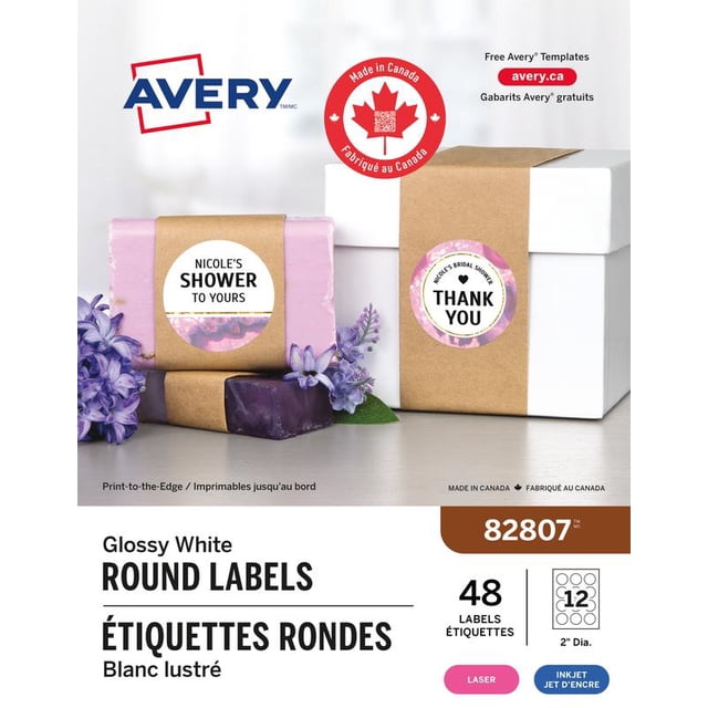 Avery Glossy White Round Labels, 2 inch diameter, shown on a lavender soap bar and a white gift box wrapped with brown kraft paper, featuring custom printed text 'Nicole's Shower to Yours' and 'Thank You' with a pink floral border, suitable for laser and inkjet printers, made in Canada, ideal for product and gift labeling.