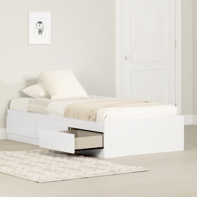 South Shore Step One Twin Mates Bed with 3 Drawers in pure white, a platform bed with three handleless drawers including one open showing light wood interior. The bed is dressed with neutral bedding and pillows, placed on a textured beige rug in a minimalist room with a white door and framed wall art.