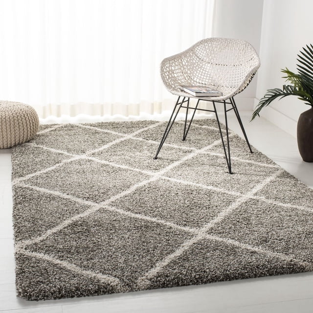 Safavieh Hudson Amias Geometric Shag Area Rug featuring a plush grey and ivory diamond tile pattern on a white floor, styled with a white woven chair and beige knitted pouf. This durable accent rug with easy-care yarns suits high traffic modern living spaces.