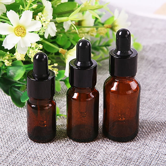 Lubelski Amber Glass Essential Oil Liquid Reagent Pipette Empty Dropper Bottle, available in sizes ranging from 5ml to 50ml. The image shows three amber glass bottles with black eye dropper caps, placed on a textured surface with a floral arrangement in the background. These bottles are ideal for storing essential oils, laboratory chemicals, perfumes, or as medicine dispensers. The amber glass provides UV protection and a professional appearance.