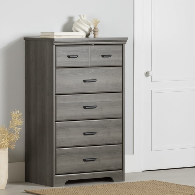 South Shore Versa 5-Drawer Chest for Adult in gray maple finish with traditional beveled edges, curved kick plate, and five spacious drawers featuring black metal handles, placed in a neutral room with a white wall, door, beige rug, and decorative vases, ideal for bedroom storage or organizing linens.
