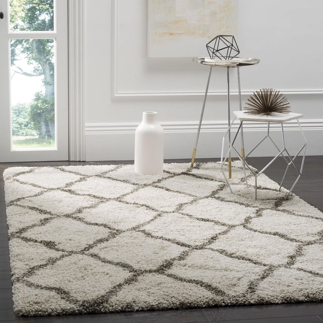 Safavieh Hudson Tapis Shag Géométrique Ligne a Mettant en Vedette une Peluche Blanche en Poils Synthétiques avec un Motif Géométrique de Carreaux Marocains Gris, Posé sur un Plancher de Bois Franc Foncé dans une Pièce Minimaliste avec un vase en Céramique Blanc et des tables d'Accent Géométriques en Métal, Convient pour Ajouter de la texture et de la Chaleur aux Zones de Tapis d'Accent.