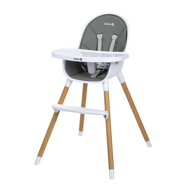 Safety 1st Avista Highchair with Scandinavian design featuring a white plastic frame, natural wood legs with white tips, and a removable grey vegan leather seat pad with safety harness. Includes a three-position adjustable white dining tray and footrest for easy cleaning and child comfort.