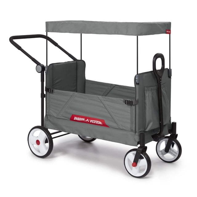 Radio Flyer Compass Stroll 'N Wagon® stroller wagon in grey with foldable UV protection canopy, black fold-away push handle, front pull handle, white wheels with red centers, fabric body with side storage pockets, and safety harness slots.