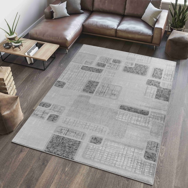 Rug Branch Sakarya Collection Tapis d'Intérieur Géométrique Moderne Abstrait en Tons Gris avec rectangles Texturés Superposés et Grilles, Fabriqué en Polypropylène durable avec une Hauteur de Poil de 0,3 Po, Exposé sur un Plancher de Bois Franc Foncé dans un Salon avec un sofa Sectionnel en Cuir Brun, une table d'Appoint en Bois et des Plantes.