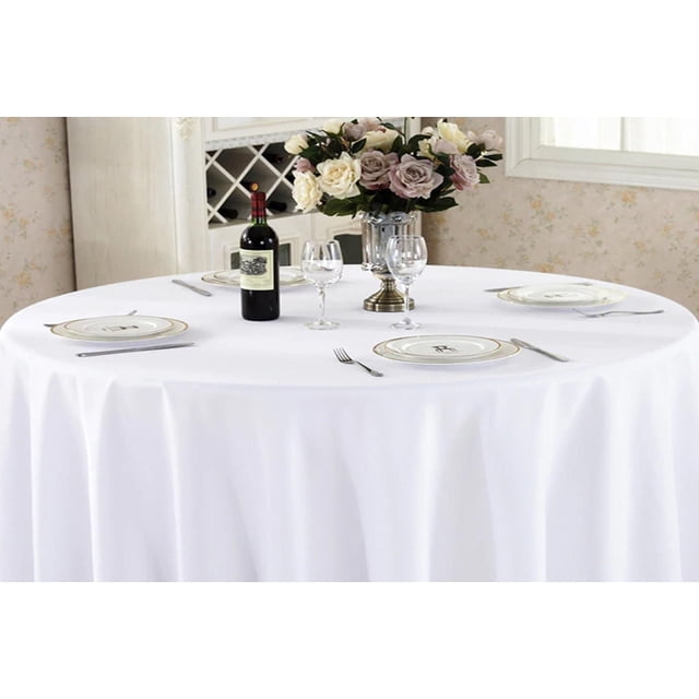 Fabstyles Hotel 100% Cotton Solid Table Cloth covering a round dining table set for four with white and gold-rimmed plates, silver cutlery, two wine glasses per setting, a bottle of red wine, and a silver vase with cream and blush roses, ideal for dinner parties, weddings, and everyday use.