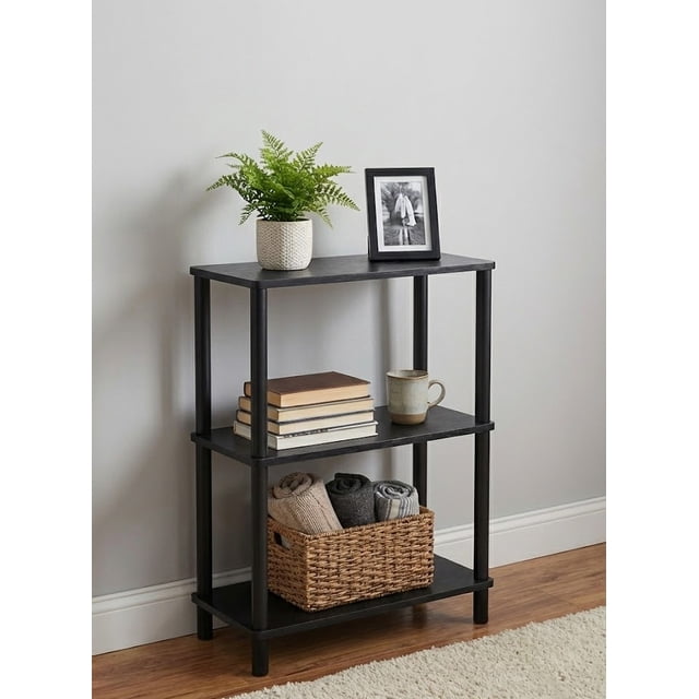 Unité d'Étagères Ouverte à 3 Niveaux avec Fini Noir, Comprenant Trois Tablettes Spacieuses pour un Rangement Ou une Présentation Polyvalents. l'Unité Est Présentée dans un Décor Moderne, Tenant des Livres, une photo Encadrée, une Plante en Pot et un Panier Tressé avec des Serviettes Roulées. Fabriquée en Bois MDF Robuste, Elle Offre une Portabilité Légère et un Assemblage Facile Sans Outils.