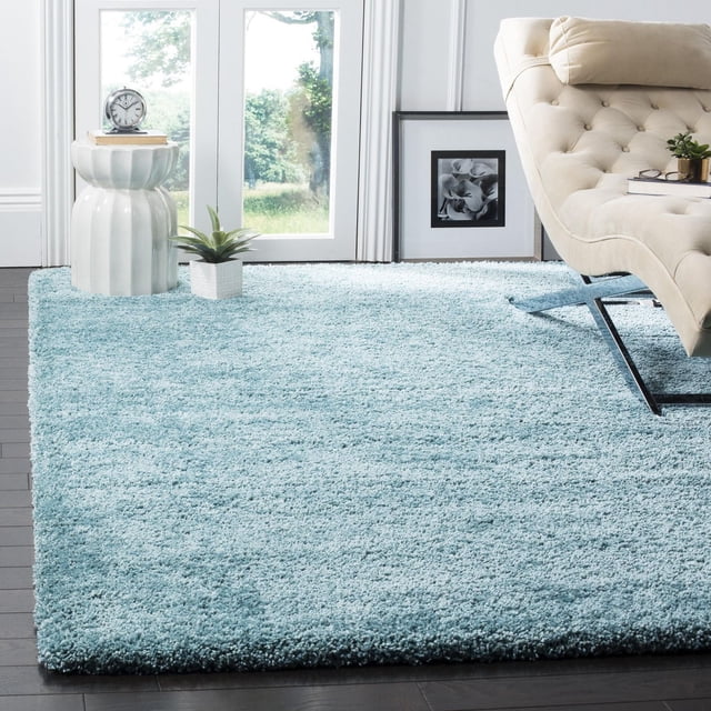 Safavieh Milan Harlow Tapis Shag Uni en Ivoire Éclatant, Montré dans une Pièce Lumineuse avec des Planchers de Bois Franc Sombres, un sofa beige Capitonné avec des Pattes en Métal, une table d'Appoint en Céramique Blanche avec une Horloge et des Livres, et une Petite Plante en Pot, Mettant en Valeur la texture en Fil Synthétique Peluche Rug's et Son Utilisation comme accent Doux pour la Déco Contemporaine de la Maison.