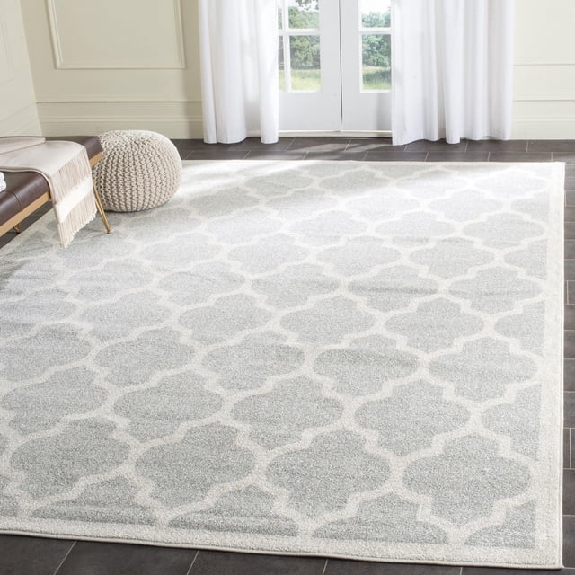 Safavieh Amherst Roderick Geometric Area Rug with a light grey and off-white geometric trellis pattern in soft cut pile polypropylene, displayed on dark tile flooring in a bright room with white curtains and a knitted pouf, ideal as an easy-care accent rug for high-traffic indoor or outdoor areas.