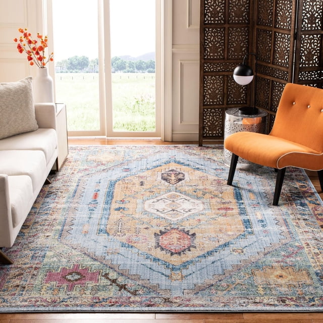 SAFAVIEH Bristol Leola Traditional Area Rug with a distressed antique-style hexagonal medallion pattern in muted blue, beige, and rust tones. Placed on hardwood flooring in a bright living room featuring a white sofa, orange accent chair, decorative vase with orange flowers, and a carved wooden folding screen. Often used to add vintage charm to modern home décor.