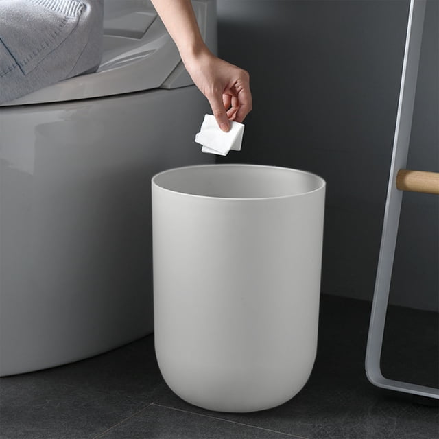 LSLJS Bathroom Trash Can in a sleek gray color, made of durable plastic with a round, thickened design. Measuring 27x20x20cm (10.63x7.87x7.87in), this large-capacity garbage bin is shown in a bathroom setting next to a toilet. A hand is seen disposing of a tissue into the lidless trash can, highlighting its easy-to-use design. Suitable for bathrooms, living rooms, offices, and other compact spaces.