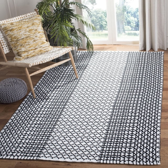 Safavieh Montauk Cara Tapis Géométrique pour Aire avec construction en Coton Tissé à Plat et Motif de Rayures Géométriques Noir et Blanc, Exposé sur un Plancher de Bois Franc à Côté d'Une Chaise Tissée avec un Coussin Jaune et une Plante Verte Près d'Une Fenêtre Éclairée par le Soleil, Convenant aux décor Côtier et Contemporain.