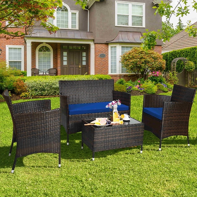 Costway 4PCS Rattan Patio Furniture Set Cushioned Sofa Chair Coffee Table Navy arranged in a vibrant garden. The set features two single chairs, a loveseat, and a tempered glass coffee table, all crafted with weather-resistant rattan and navy cushions for comfort. This outdoor conversation set is perfect for patios, porches, or poolside relaxation.