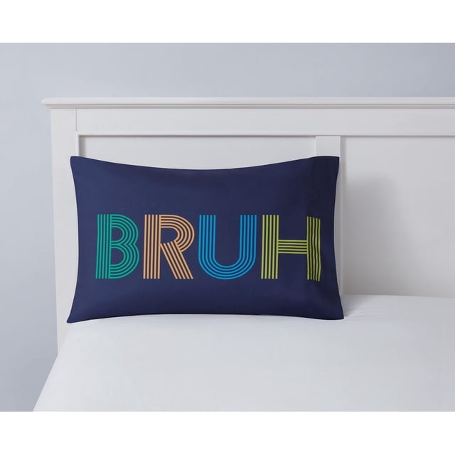 Mainstays Kids Printed Pillowcase 1 piece in navy blue with the word 'BRUH' printed in large multicolored striped letters in green, orange, blue, and yellow, displayed on a white bed with a white headboard, suitable for kids bedding and adding a playful touch to a child's room.