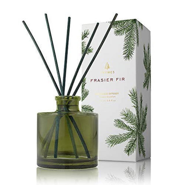 Thymes Frasier Fir Diffuseur de Petites Roses avec un Contenant en Verre Vert et des Bâtonnets de Roseaux Noirs, Conçu pour Remplir les Espaces Douillets du Parfum Net d'Aiguilles de Sapin de Sibérie, de Cèdre et de Bois de Santal. le Produit Est Exposé aux Côté de Son Emballage Décoratif Orné d'Illustrations de Branches de Sapin.