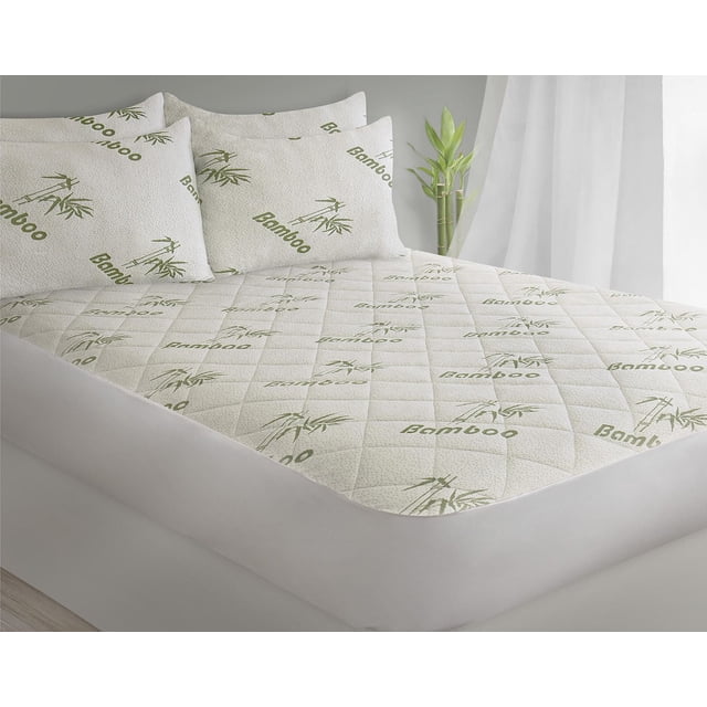 Safdie & Co. Mattress Protector T Bamboo Jacquard twin size with quilted white surface printed with green bamboo leaves and text, fitted on a bed with white base and pillows, featuring waterproof, hypoallergenic fabric ideal for allergy protection, in a softly lit room with sheer curtains and a bamboo plant.