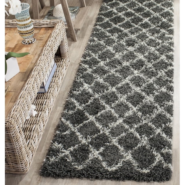 Safavieh Dallas Jerrie Tapis Shag Géométrique avec Motif Losange dans des Tons Gris Foncé et Clair sur un Plancher de Bois Clair à Côté d'Une Étagère en Osier avec Déco. Ce Tapis d'Accent durable et Facile d'Entretien Offre une Sensation Douce et Texturée Idéal pour les Zones à Fort Passage à la Maison Ou au Bureau.