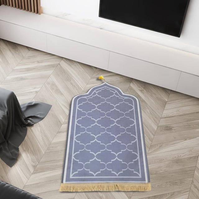 Portable Prayer Rug Praying Mat Folding Worship Carpet for Gifts Travel Home Gray. The rug is made of high-quality velvet material, featuring a soft and thick texture for comfort. It has a non-slip flannel backing for stability and is decorated with a simple, elegant geometric pattern in gray with tassels at the bottom. Measuring 65cm x 110cm (25.59 inches x 43.31 inches), it is suitable for home, bedroom, living room, or travel use. Displayed in a modern living room setting with a light wood floor.