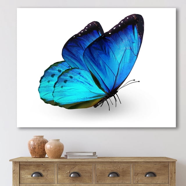 Designart Vibrant Blue Butterfly Canvas Wall Art showing a gallery-wrapped cotton canvas print of a vivid blue butterfly with black edges and white spots, stretched over a wood sub frame, displayed above a wooden console table with decorative vases and books, ready to hang in modern home décor.