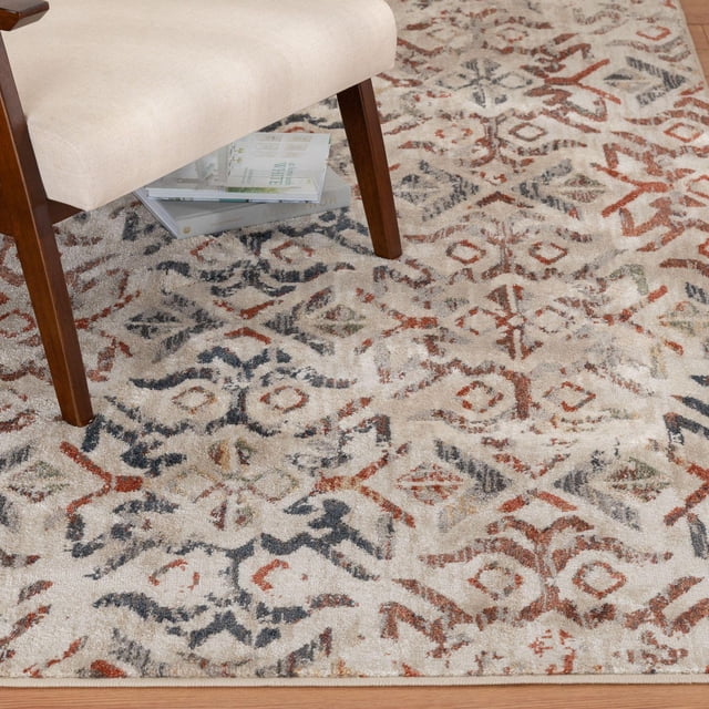 Pescara Navy Blue and Red Woven Area Rug with a distressed ornate pattern in navy blue, rusty red, and cream, shown under a beige upholstered chair with wooden legs on hardwood flooring, made from stain-resistant polypropylene with a low-profile pile suitable for living and dining areas.