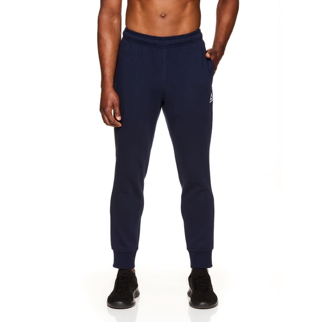 Reebok Men's Delta Fleece Jogger in navy blue with tapered legs, ribbed cuffs, and elastic waistband with branded drawcord, shown front-facing on a male model from waist to ankles. Features side pockets and the Reebok logo on the left thigh, ideal for casual or active wear.