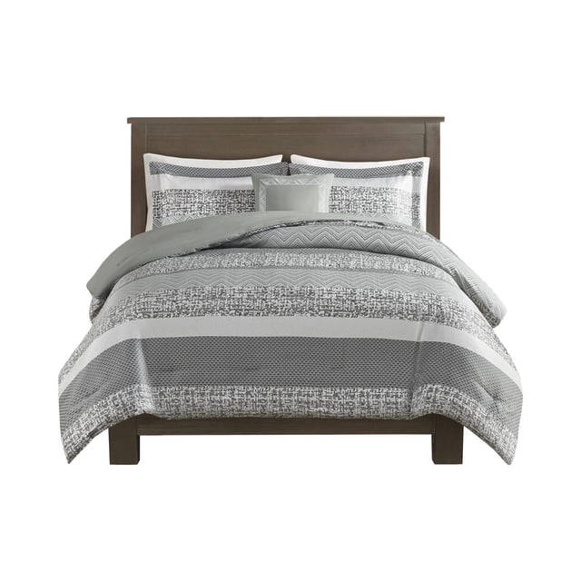 Madison Park 4 Piece Rhapsody Comforter Set on a wooden bed frame, featuring a grey and taupe woven jacquard comforter with color block stripes and varied motifs, two matching shams, and an embroidered decorative pillow, machine washable and ideal for updating bedroom bedding.