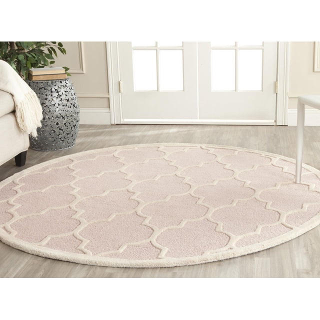 Safavieh Cambridge Kevin Geometric Area Rug, a round hand-tufted wool accent rug with a textured geometric pattern in soft beige and cream, placed on light wood flooring near white French doors in a neutral room, suitable for adding warmth and style to living spaces.