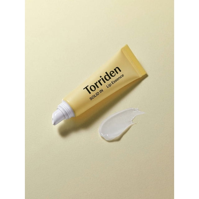 Torriden Solid-In Ceramide Lip Essence 11ml tube in pale yellow with black text, shown with a clear balm swatch on a light yellow background, a nourishing lip treatment formulated with ceramides and oils to hydrate and protect dry, chapped lips, also suitable for use as an overnight lip mask for intensive repair.