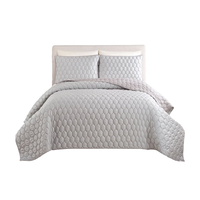 Better Homes & Gardens Quilt in light grey with circular quilted pattern, shown on a bed with matching pillow shams and beige upholstered headboard, made with a soft Tencel face and polyester fill, available in Full/Queen and King sizes, suitable for decorative layering and added warmth.