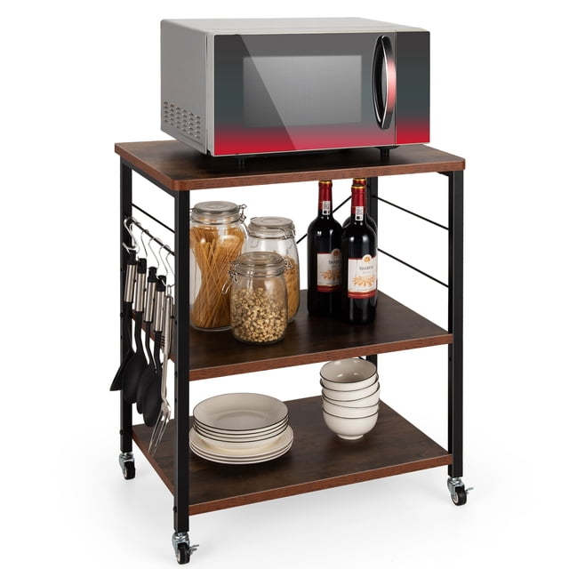 Costway 3-Tier Kitchen Baker's Rack Microwave Oven Storage Cart with hooks in a rustic brown finish. The cart features three spacious tiers for storage, including a top shelf holding a microwave, a middle shelf with jars and wine bottles, and a bottom shelf with stacked plates and bowls. Ten side hooks hang cooking utensils, and the cart is supported by a sturdy black iron frame with X-shaped reinforcement. Equipped with four caster wheels, two of which are lockable, for easy mobility and stability.