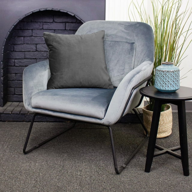 Housse de Coussin de Luxe Franklin en Gris avec Fermeture Éclair, Exposée sur un Fauteuil en Velours Gris Pâle avec Pattes en Métal Noires, à Côté d'Une table d'Appoint Ronde Noire Tenant un vase en Céramique Bleu Texturé, avec un Cache-Pot en Panier Tressé et une Haute Herbe Verte en Arrière-Plan, Idéale comme Housse de Coussin Décorative pour la Déco de la Maison.