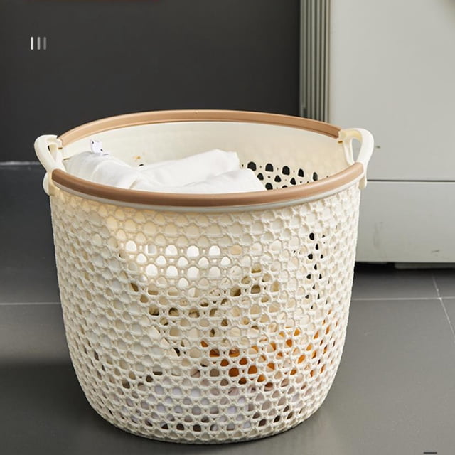 Suncoda Laundry Basket, a portable and hollow plastic basket with a beige finish and sturdy handles, ideal for laundry room storage and organizing dirty clothes, towels, bedding, and toiletries. The breathable open design enhances airflow, and the basket is shown placed on a tiled floor near a cabinet.