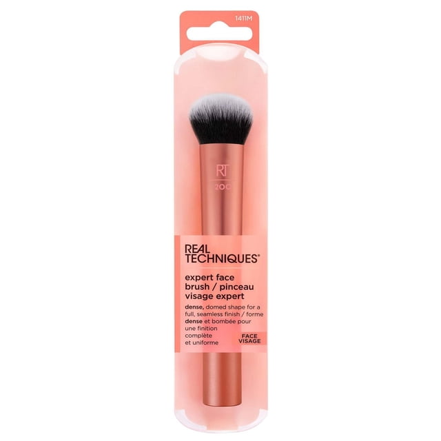 Real Techniques Expert Face Brush with dense, domed synthetic bristles and rose gold aluminum ferrule, designed for seamless blending of liquid and cream foundations, shown in pink and clear retail packaging with bilingual English and French text.