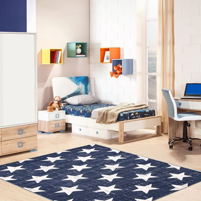 ECARPET Kids Room, Nursery, Playroom, Bedroom Area Rug, Angel Collection with a navy blue rug featuring white stars on light wood flooring in a child's bedroom. The room includes a bed with a wave-themed headboard, a nightstand with a stuffed monkey, colorful wall-mounted cube shelves, and a desk with a blue chair. Made from ultra-soft yarn, this durable rug suits high-traffic kids' rooms and is pet-friendly, often used to add a modern graphic art vibe to play areas.
