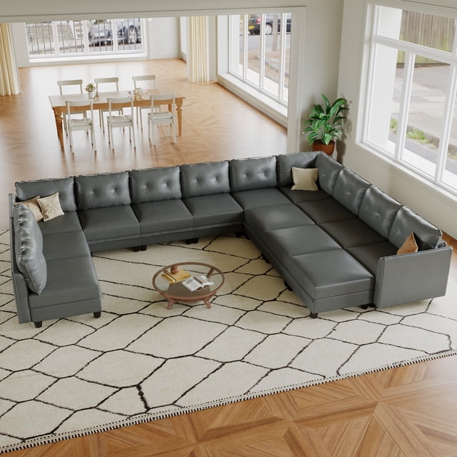 LLappuil Modular Sectional Sofa, a 14-seat oversized modular sectional sofa in grey faux leather, displayed in a spacious living room. The sofa offers customizable configurations, including L-shaped and U-shaped layouts, with reversible ottomans for footrests or additional seating. Hidden storage compartments in each module enhance functionality. Ideal for living room seating, the faux leather upholstery is waterproof and durable, suitable for residential use.