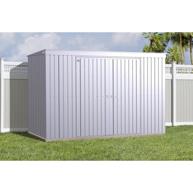 Arrow Elite Steel Storage Shed, 10x4, Galvalume, front view showing a rectangular metal shed with squared vertical wall panels, tall 72-inch walls, and double reinforced swing doors with brushed nickel key lock handles, set on green grass with white vinyl fencing and palm trees in the background under a partly cloudy sky, ideal for backyard storage or garden tools
