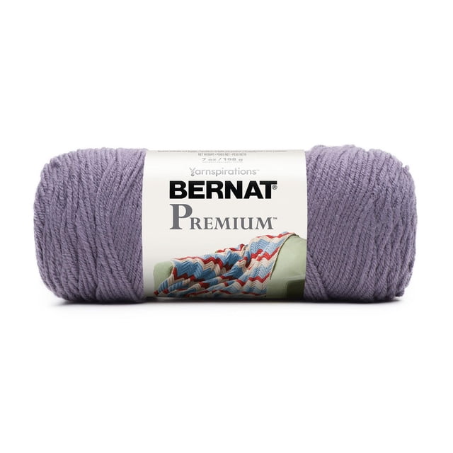 Bernat® Premium TM Fil, Acrylique #4 Moyen, 7oz/198g, 360 Yards en Lavande, Montré comme un Écheveau Bien Enroulé avec une Étiquette Blanche Présentant le logo Bernat Premium et une image d'Un afghan Crocheté sur un Canapé Vert, Convient aux Projets de Tricot et de crochet Incluant des Vêtements et la Déco Maison.